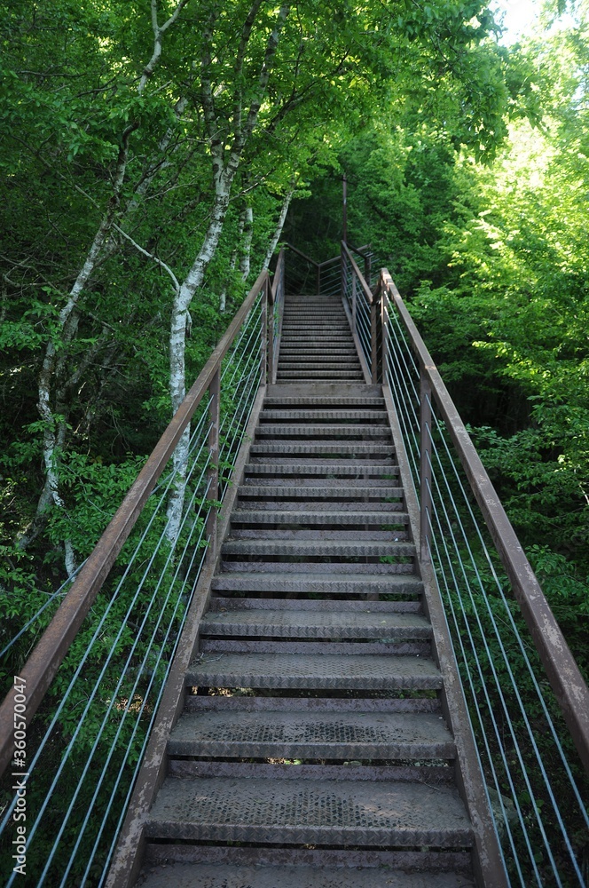 Metal staircase with railing on the green slope of the mountain leading up