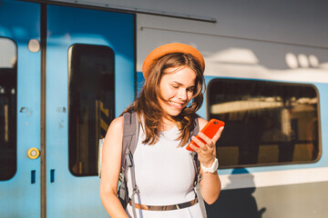 Smiling woman using smart phone on station. Young woman holding smartphone and standing at train station. Theme Transportation And Travel. trip journey travel concept