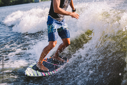 Active wakesurfer jumping on wake board down the river waves. Surfer on wave. Male athlete training on wakesurf training. Active water sports in open air on board. A man catches a wave on surf © Elizaveta