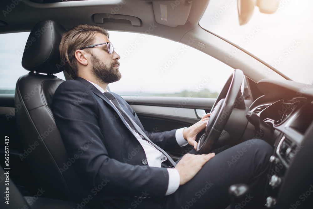 Side view of serious bearded man dressed in formal clothing driving car to business meeting. Mature businessman in eyeglasses fastened with seatbelt in auto. Side view of serious bearded man dressed in formal clothing driving car to business meeting. Mature businessman in eyeglasses fastened with seatbelt in auto.