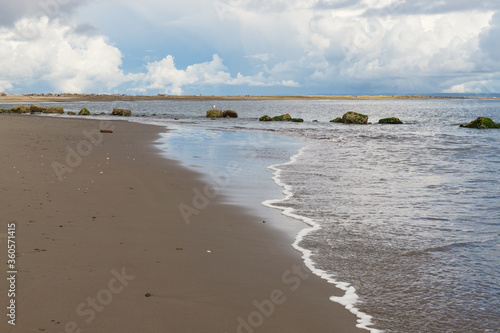 Fototapeta Naklejka Na Ścianę i Meble -  Ocean Wave on Sandy Beach with Large Rocks in Background