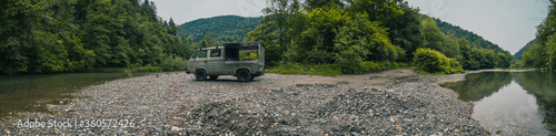 Old vintage custom offroad campervan is parked in the morning hours on the shores of a lazy river on a stone embankment. Adventurous night with a car