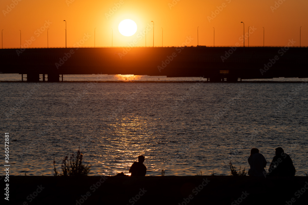 Fototapeta premium Silhouettes of people enjoying seascapes on the shore during sunset.