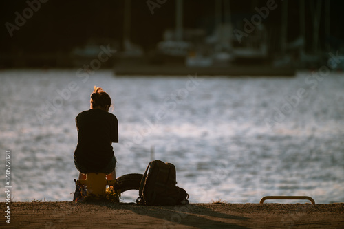 Alone female sitting on a bollard at the shore looking at the sunset.