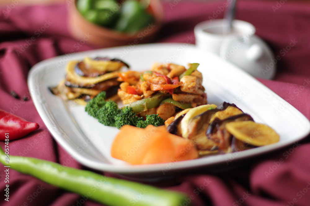 Fried chicken with vegetables. Pepper, broccoli, eggplant, paprika and potatoes. A dish on a red background.