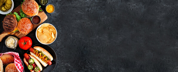 Summer BBQ food side border with hot dog and hamburger buffet. Top down table scene over a dark slate background. Copy space.