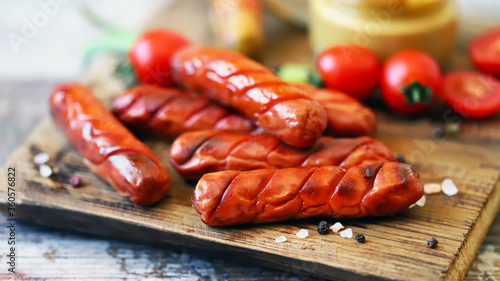 Appetizing fried smoked sausages on a wooden board. Sausages with spices and mustard. German appetizer. Beer snack.