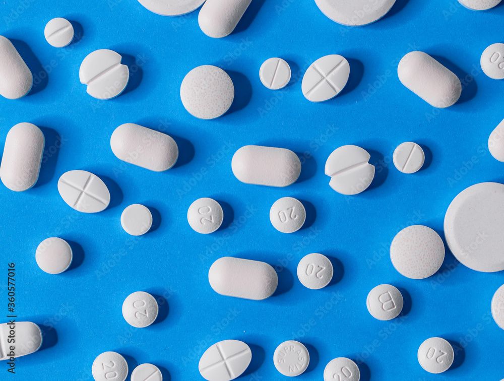 many different pills  scattered on a blue paper background, close-up top view.