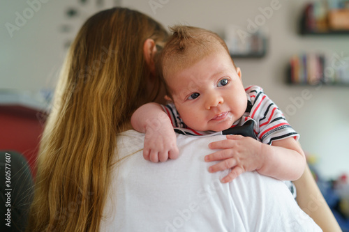 Tablou pe pânză Mother holds her two moths old baby on the shoulder at home - Caucasian woman wi