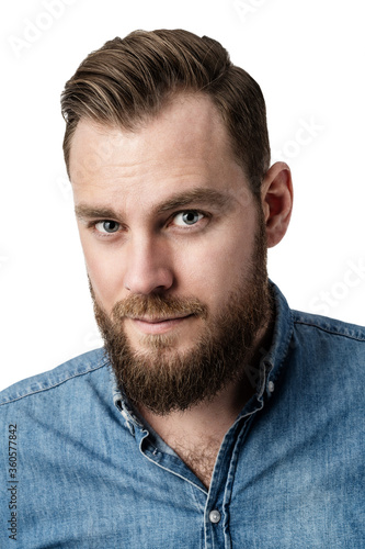Handsome brownhaired guy with a nice beard and pretty eyes wearing ablue denim shirt looking pensively towards the camera against a white background. photo