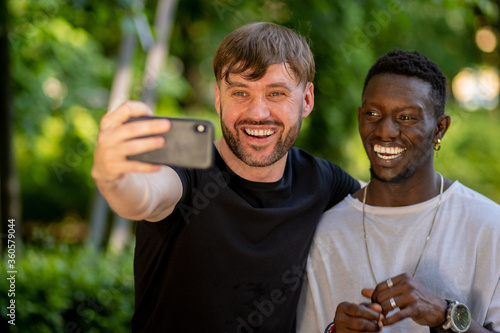 A black man and a white man take a selfie on their smartphone and laugh. Interracial friendship