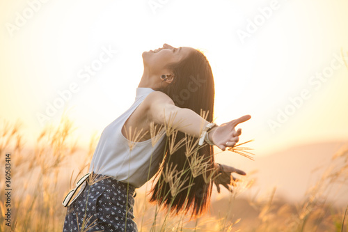 free happy woman enjoying sunset. Beautiful woman in white dress embracing the golden sunshine glow of sunset with arms outspread and face raised in sky enjoying peace, serenity in nature photo