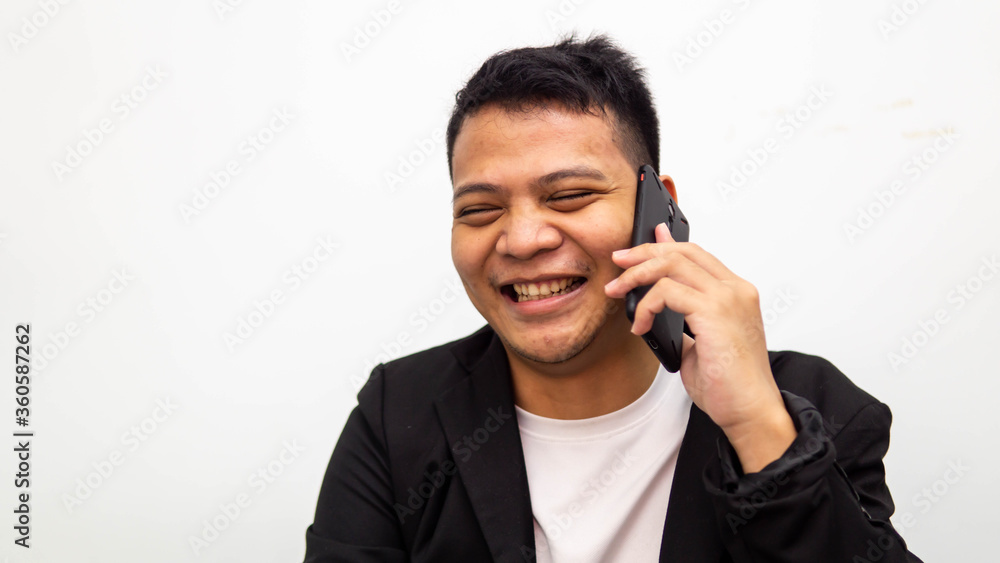 A portrait of happy young Asian businessman laughing while talking and having conversation on the phone with isolated white background. Career business job concept. A portrait of happy young Asian businessman laughing while talking and having conversation on the phone with isolated white background. Career business job concept.
