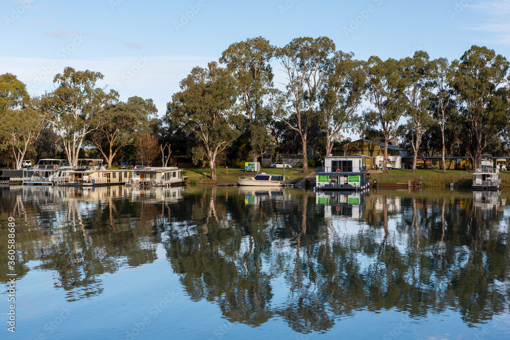 The reflection of house boats and tree on a calm river murray located in the river land at Berri South Australia on 20th June 2020