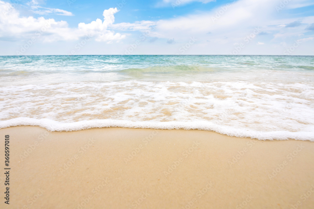 Soft ocean wave on sandy beach with blue sky.