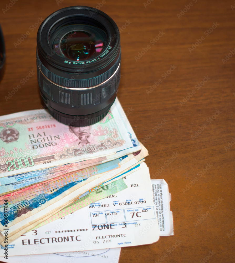 Camera lens, foreign money and aircraft boarding pass on a wooden table. Tourism, vacation, travel photography equipment.