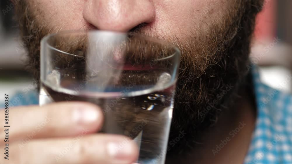 Bearded man drinks sparkling drinking water. Male hand holds glass to his mouth and drinks mineral water Bearded man drinks sparkling drinking water. Male hand holds glass to his mouth and drinks mineral water