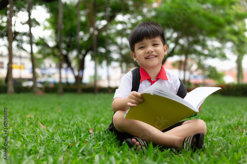 Cute little child reading a book on green grass in park