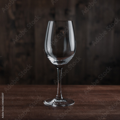 Empty wine glass on wooden table against dark background in bar. Crystal clear wine glass with traditional round goblet shape and slim stem on wood counter top bar with blurry background scene