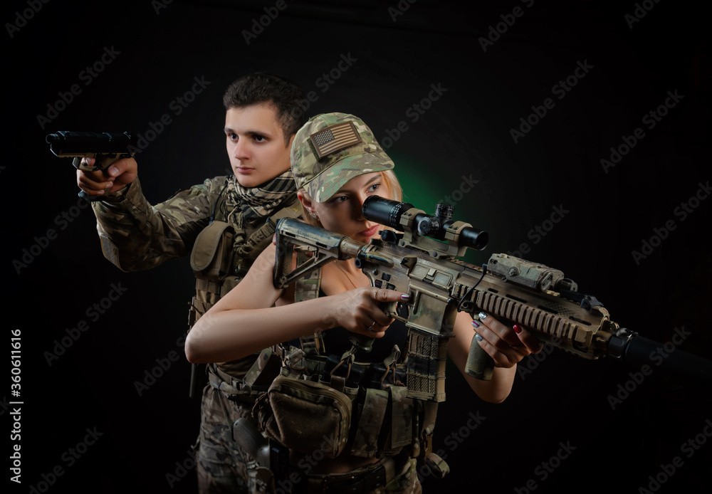 a girl and a guy in military overalls pose with an airsoft gun on a dark background
