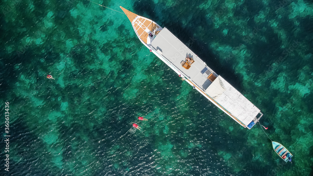 aerial shot of beautiful blue lagoon at hot summer day with diving boat. Top view of people are swimming around the boat. aerial shot of beautiful blue lagoon at hot summer day with diving boat. Top view of people are swimming around the boat.