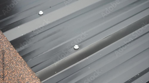 Closeup hands of worker installing the metal sheet roof by using the electrical drilling tool.