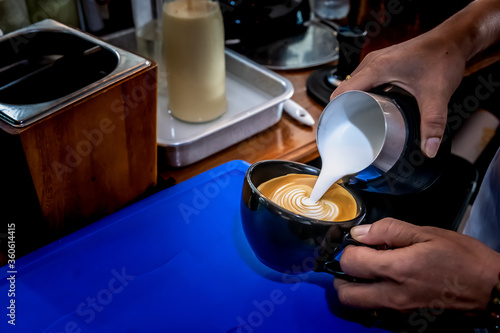 Barista pouring milk in coffee cup for make cappuccino art.