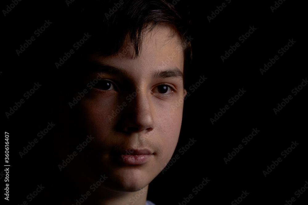 Portrait of a teenager on a black background. The boy has dark hair Portrait of a teenager on a black background. The boy has dark hair