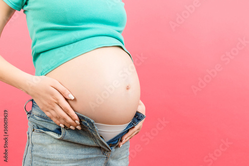 Cropped image of pregnant woman in unzipped jeans showing her baby bump at colorful background with copy space. Waiting for a baby concept