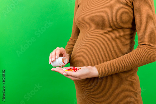 Close up of pregnant woman taking a pile of pills from a bottle at colorful background with copy space. Health care during pregnancy concept