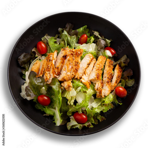 Grilled chicken breast and salad served on black plate on white background.