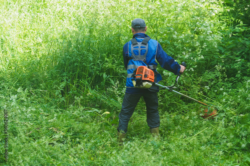 Man mows tall grass with a manual lawn mower