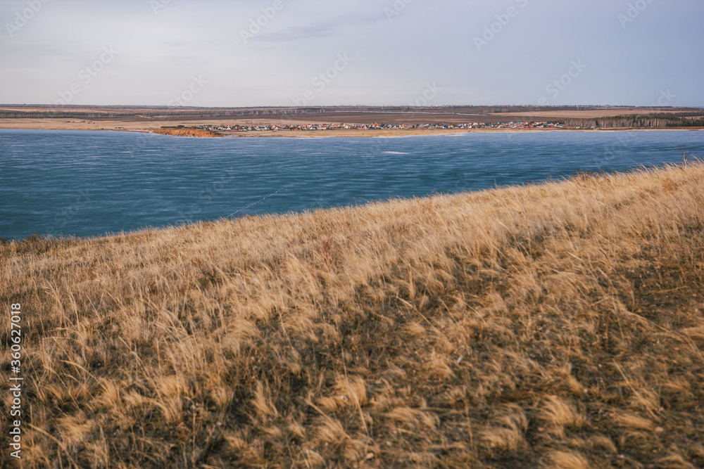 
View from a hill with dry grass to a frozen lake without snow