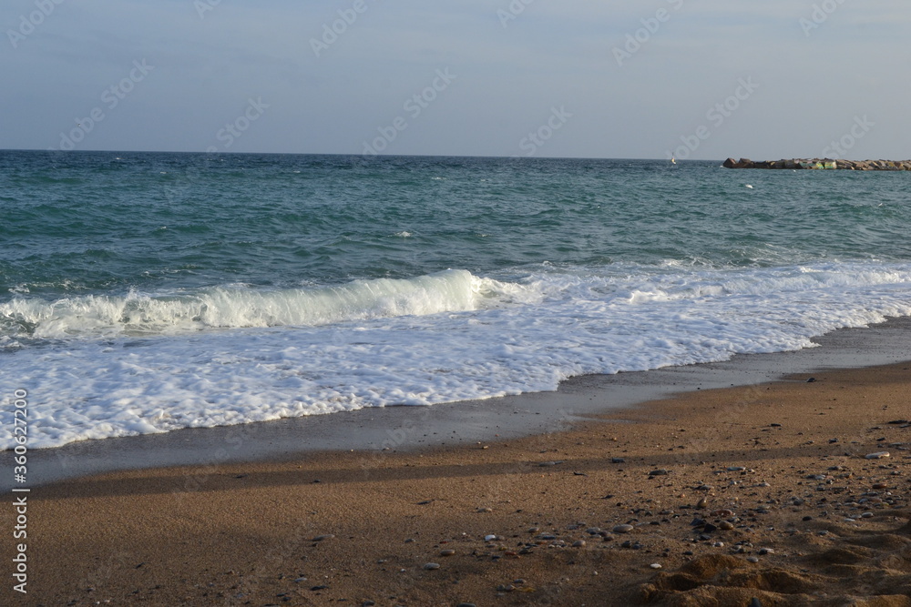small waves of the Mediterranean Sea roll ashore from pebbles and stones in the afternoon