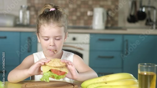 Portrait of a cute girl in kitchen takes a fresh Burger from the table with grilled meat tomato cheese lettuce sesame bun. A happy Child eats a hamburger. cooking a Burger and sandwich on the grill