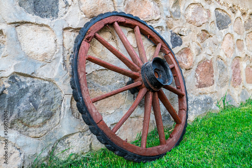 Wooden wagon wheel leaning against old stone wall