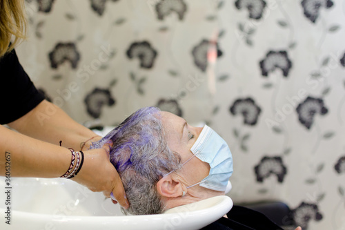 Mujer con canas en una peluquería mientras la peluquera le lava el pelo