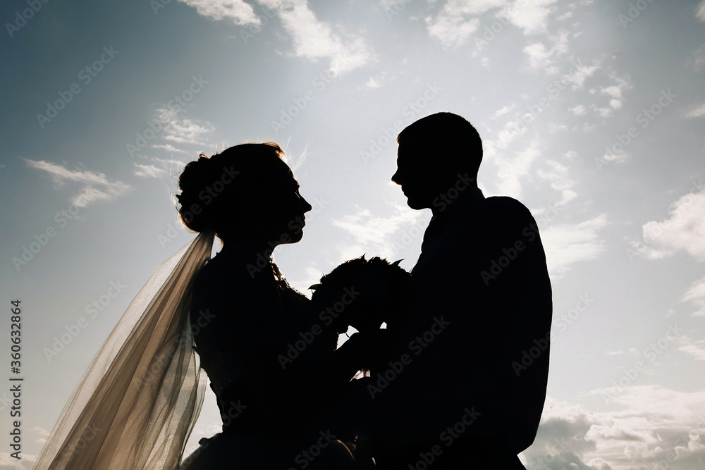 silhouette of a wedding couple holding a bouquet on a background of blue summer sky