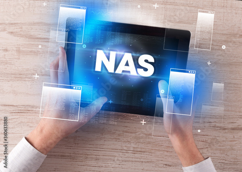 Close-up of a hand holding tablet with NAS abbreviation, modern technology concept