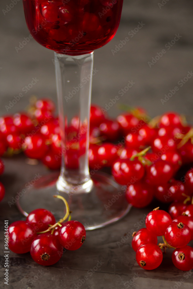 Red currant in a shot glass, the rest is scattered around it on a gray textured background Red currant in a shot glass, the rest is scattered around it on a gray textured background