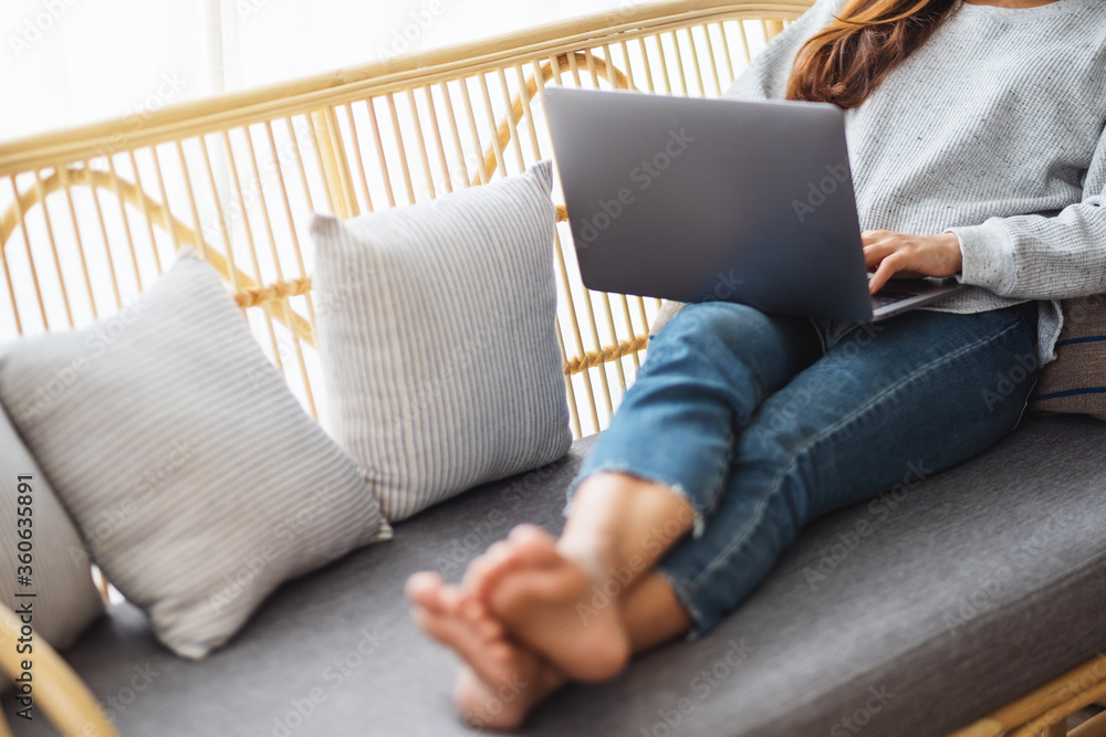 Closeup image of a young woman using and working on laptop computer while lying on a sofa at home Closeup image of a young woman using and working on laptop computer while lying on a sofa at home