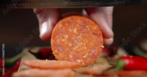 Male hand with large knife cut the salami on a cutting Board.