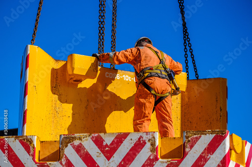 Canvas Print Worker in orange suite and hard hat positions heavy counterweight on mobile cran