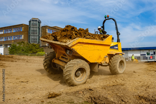 Tipper truck driven by worker in hard hat and hi-vis jacket with load of earth reverses across construction site