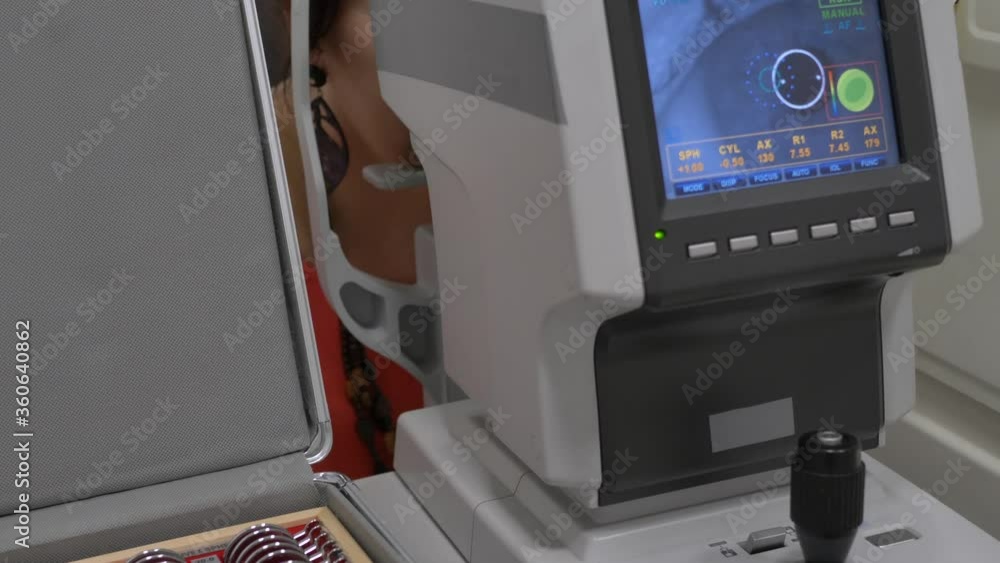 Female patient closeup eye on a eye examination modern autorefractor computer-controlled machine. Medical attendance at the optometry clinic with glasses in background Female patient closeup eye on a eye examination modern autorefractor computer-controlled machine. Medical attendance at the optometry clinic with glasses in background
