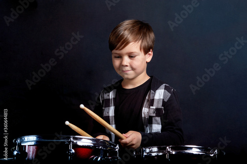 A brunette child boy plays the drums. Studying in the studio.