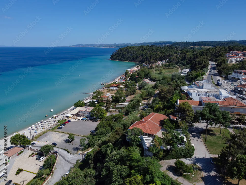 Chalkidiki, Greece coastal village landscape drone shot with pine trees. Aerial day view of Kallithea seafront at Kassandra peninsula with a beach bar by a clean tranquil blue sea.