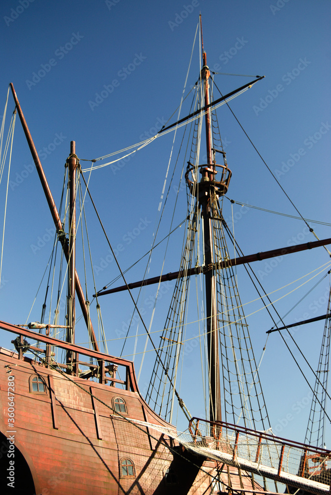 Vista lateral e de parte da popa de um navio pirata com as velas recolhidas, mastro principal com cesto para o vigia observar o horizonte, escadas em corda