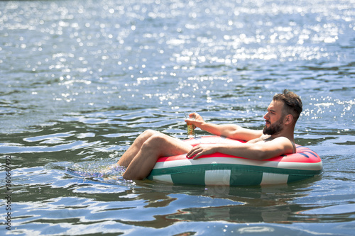 the guy floats on an inflatable circle on the river, in his hands he has a glass of beer