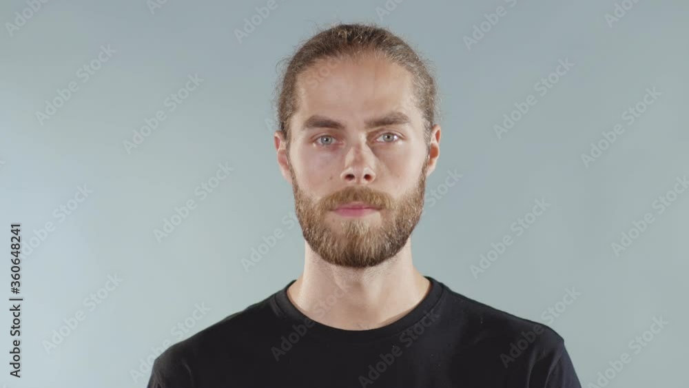 Attractive young serious man look at camera on grey background face t-shirt close up slow motion Attractive young serious man look at camera on grey background face t-shirt close up slow motion